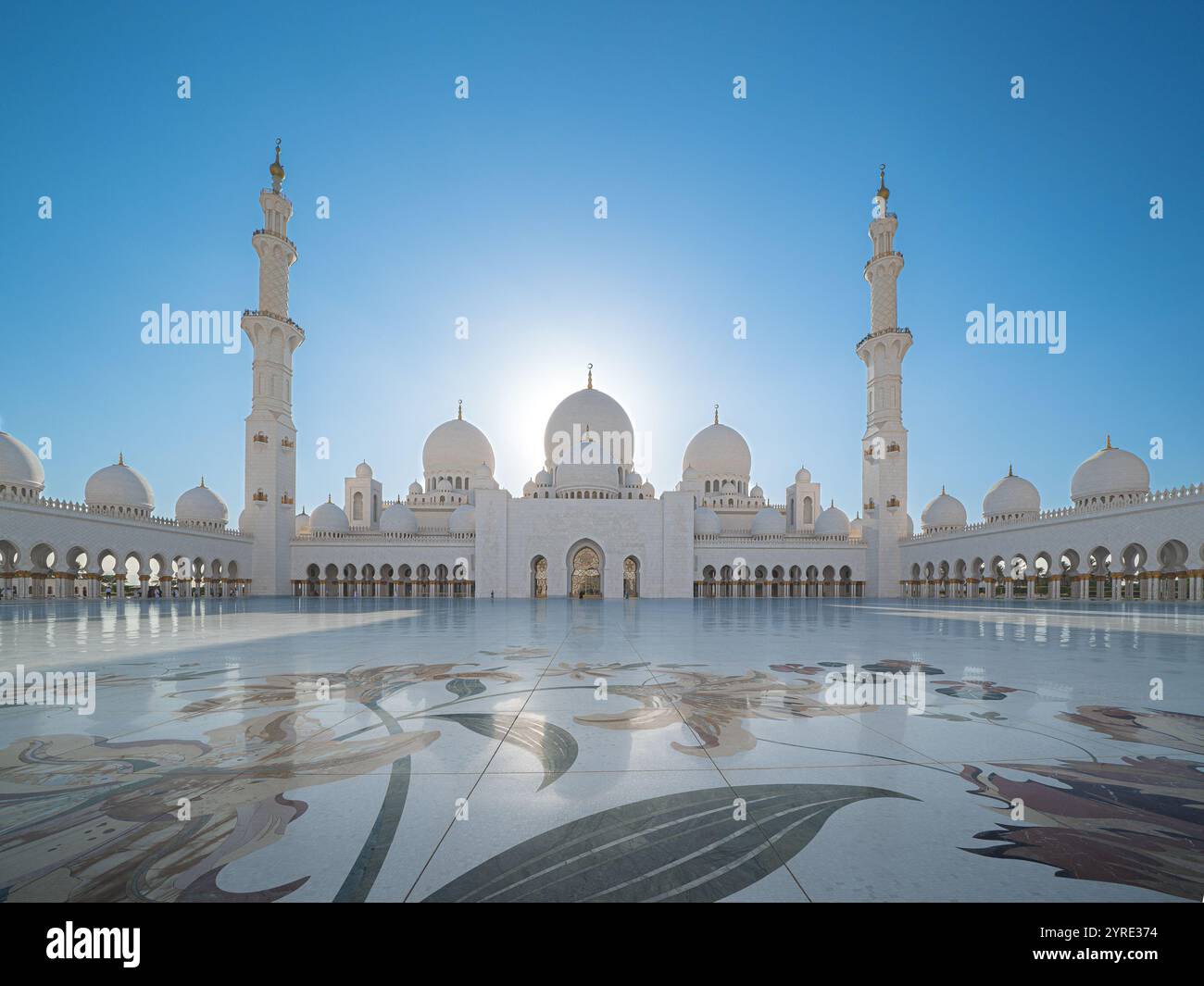 Grande Moschea dello Sceicco Zayed, Abu Dhabi, caratterizzata da intricati disegni floreali sul cortile in marmo con grandi cupole e minareti che brillano sotto una chiara b Foto Stock