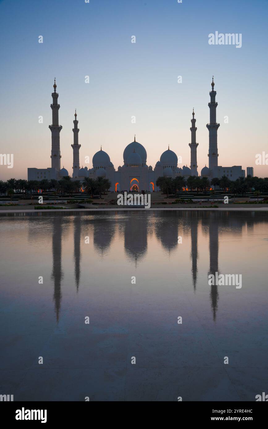 Grande Moschea dello Sceicco Zayed al crepuscolo con tranquilli riflessi d'acqua e un morbido cielo pastello, che mostra cupole e minareti iconici ad Abu Dhabi Foto Stock