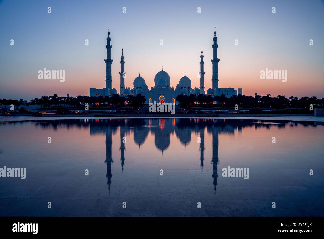 Grande Moschea dello Sceicco Zayed illuminata al crepuscolo con la sua serena riflessione sull'acqua, che mostra maestose cupole e minareti ad Abu Dhabi Foto Stock