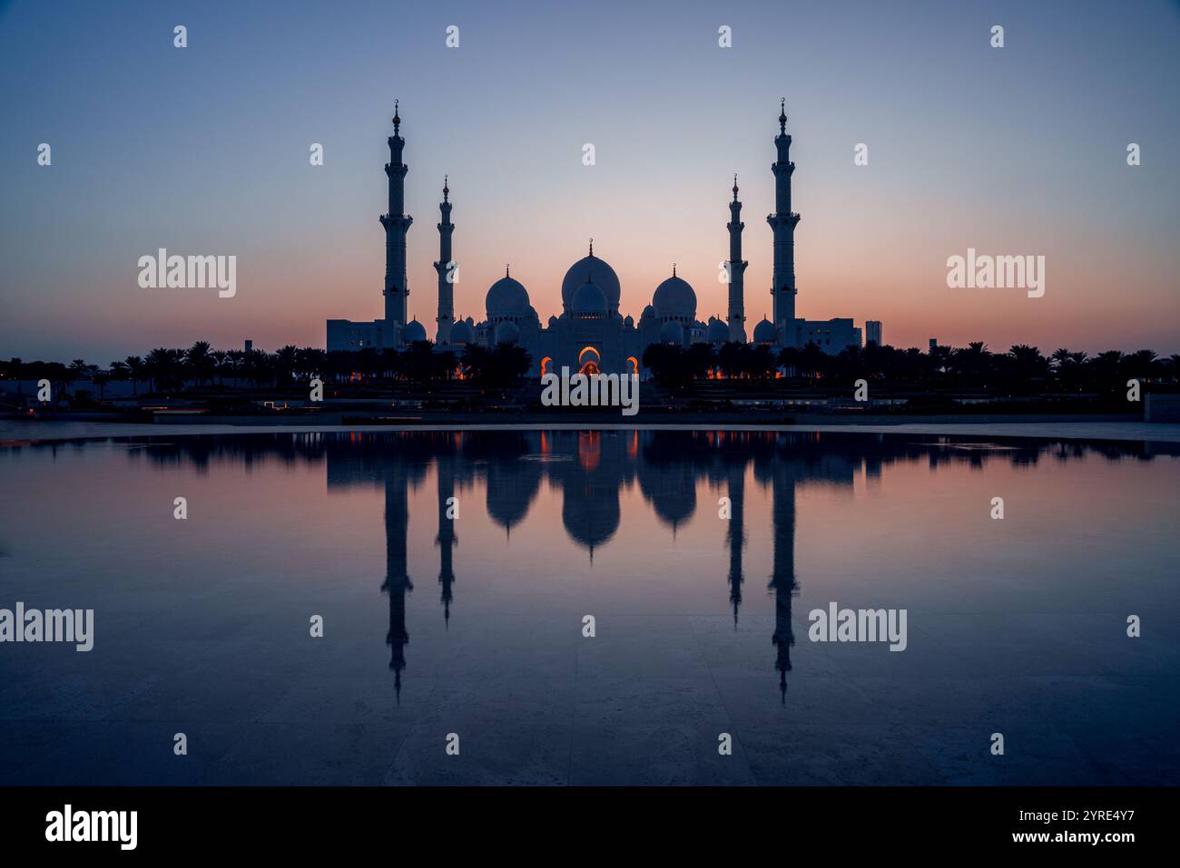 Grande Moschea dello Sceicco Zayed illuminata al crepuscolo con la sua serena riflessione sull'acqua, che mostra maestose cupole e minareti ad Abu Dhabi Foto Stock