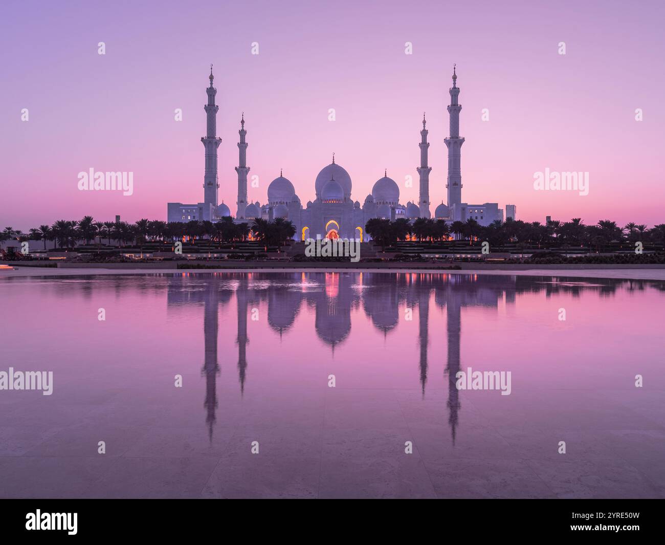 La grande Moschea dello Sceicco Zayed risplende nelle tenui sfumature rosa dell'alba, che si riflette sulle acque tranquille, mostrando cupole e minareti iconici di Abu Dhabi Foto Stock
