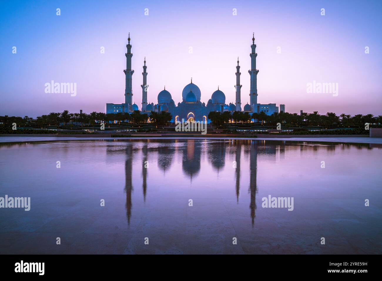 Grande Moschea dello Sceicco Zayed illuminata al crepuscolo con la sua serena riflessione sull'acqua, che mostra maestose cupole e minareti ad Abu Dhabi Foto Stock