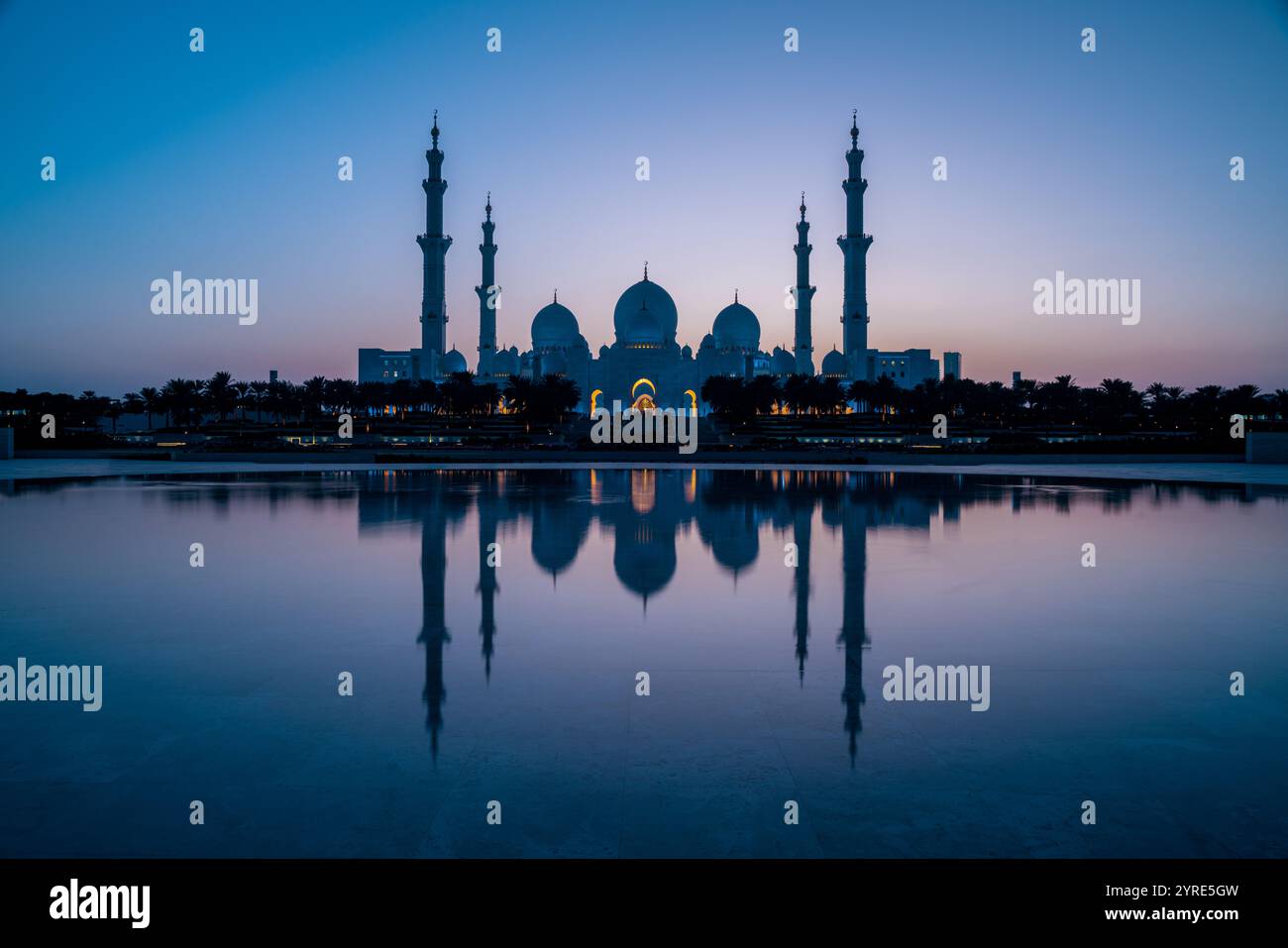 Grande Moschea dello Sceicco Zayed illuminata al crepuscolo con la sua serena riflessione sull'acqua, che mostra maestose cupole e minareti ad Abu Dhabi Foto Stock