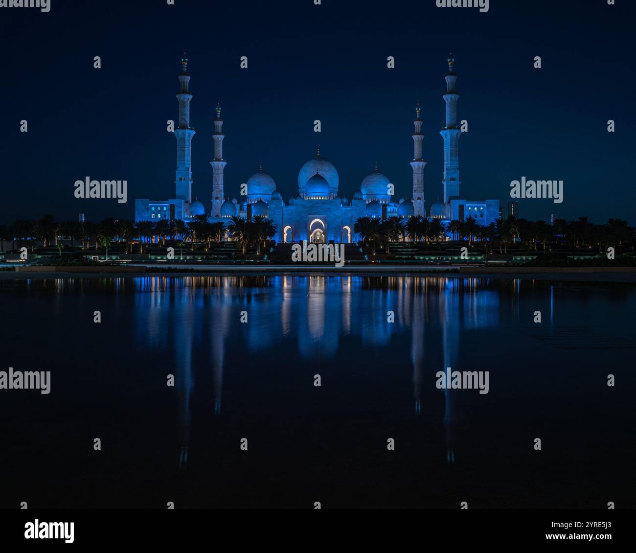 La grande Moschea dello Sceicco Zayed è illuminata di blu vibrante durante la notte, riflettendo sulla tranquilla superficie dell'acqua. Un capolavoro di architettura islamica. Foto Stock