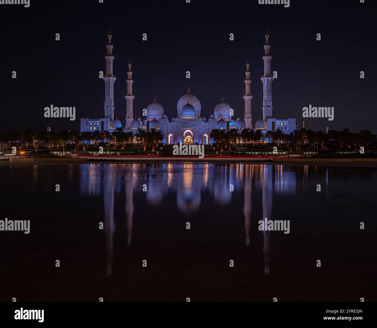 La grande Moschea dello Sceicco Zayed, illuminata di luce viola di notte, si riflette splendidamente in acque calme, mostrando l'eleganza architettonica islamica. Foto Stock