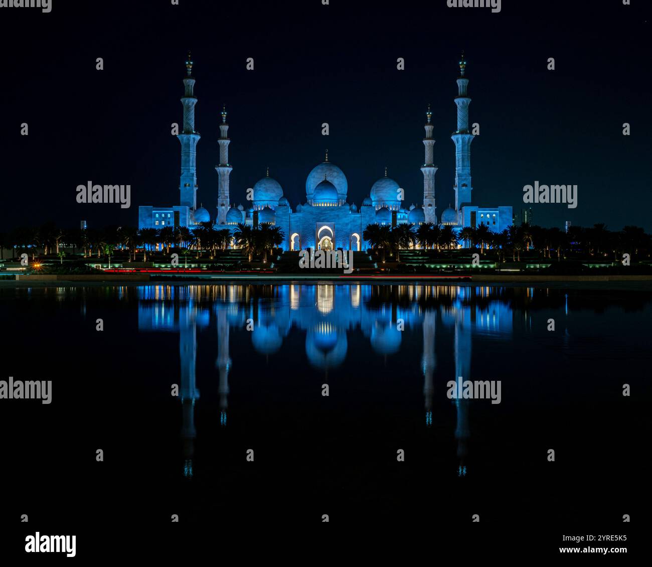 La grande Moschea dello Sceicco Zayed è illuminata di blu vibrante durante la notte, riflettendo sulla tranquilla superficie dell'acqua. Un capolavoro di architettura islamica. Foto Stock