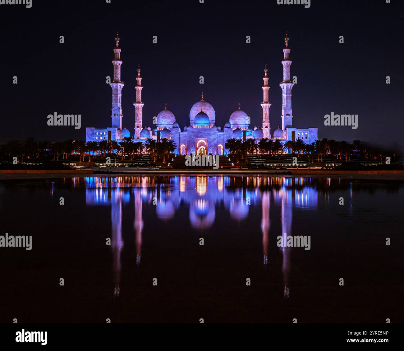 La grande Moschea dello Sceicco Zayed, illuminata di luce viola di notte, si riflette splendidamente in acque calme, mostrando l'eleganza architettonica islamica. Foto Stock