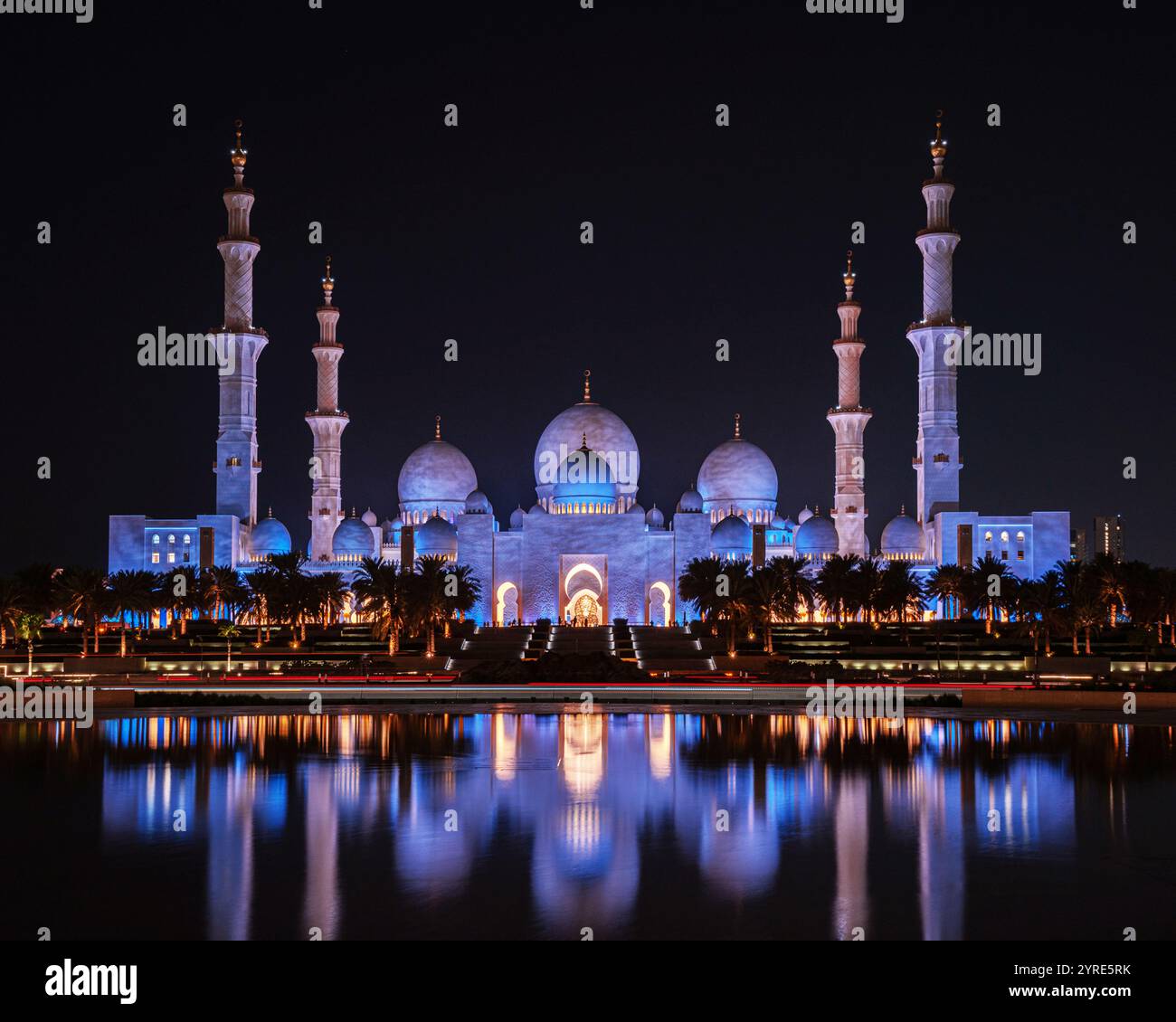 La grande Moschea dello Sceicco Zayed, illuminata di luce viola di notte, si riflette splendidamente in acque calme, mostrando l'eleganza architettonica islamica. Foto Stock