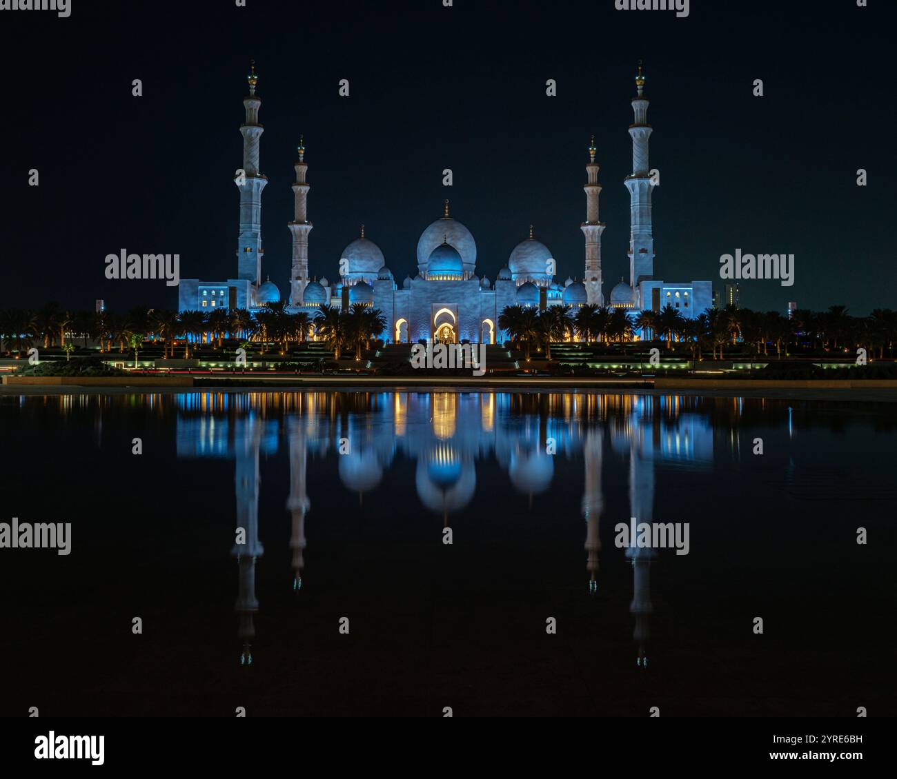 La grande Moschea dello Sceicco Zayed è illuminata di blu vibrante durante la notte, riflettendo sulla tranquilla superficie dell'acqua. Un capolavoro di architettura islamica. Foto Stock