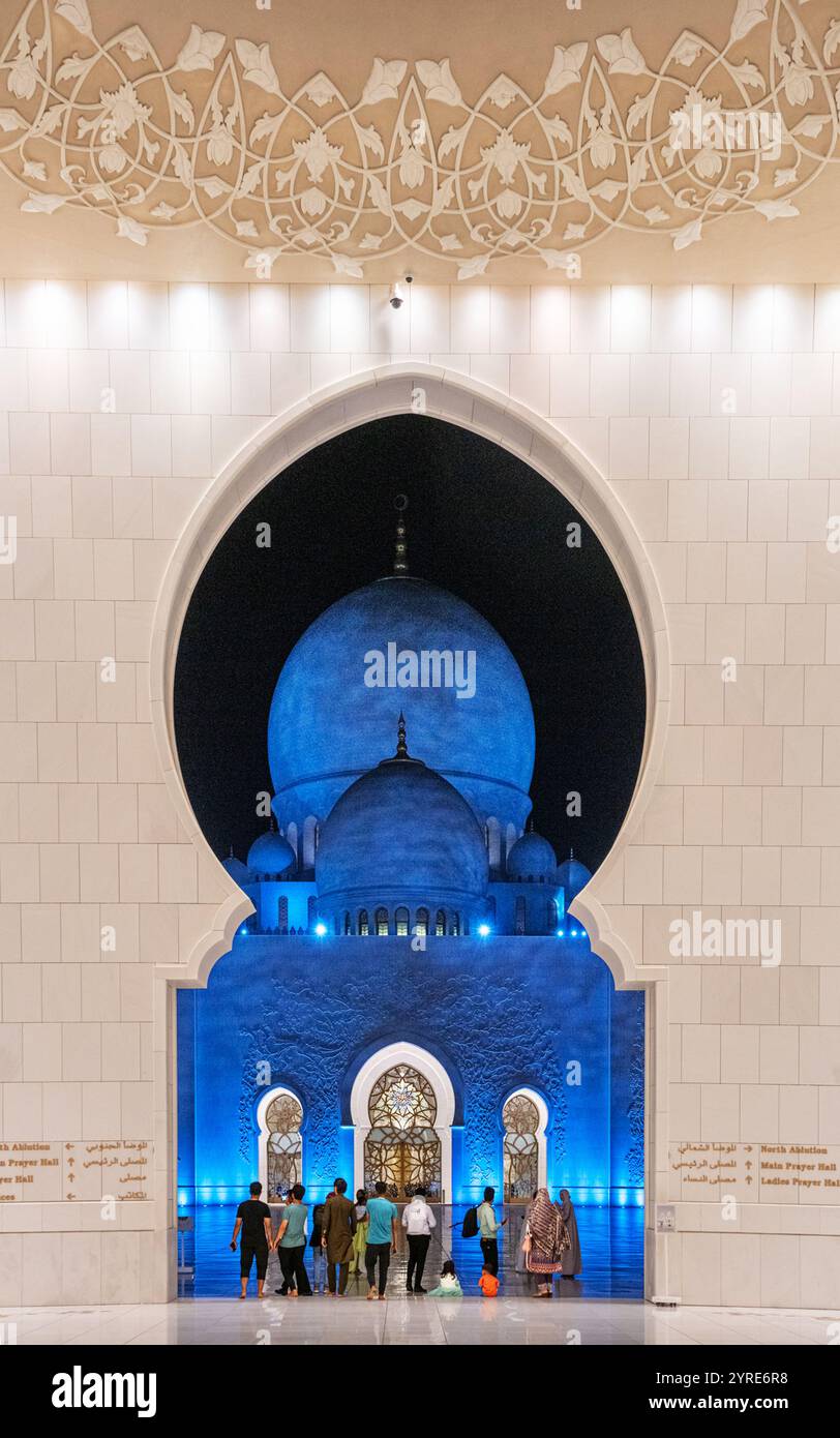 Cupole illuminate della grande Moschea dello Sceicco Zayed viste attraverso un arco ornato di notte, che mostra eleganza architettonica e atmosfera spirituale. Foto Stock