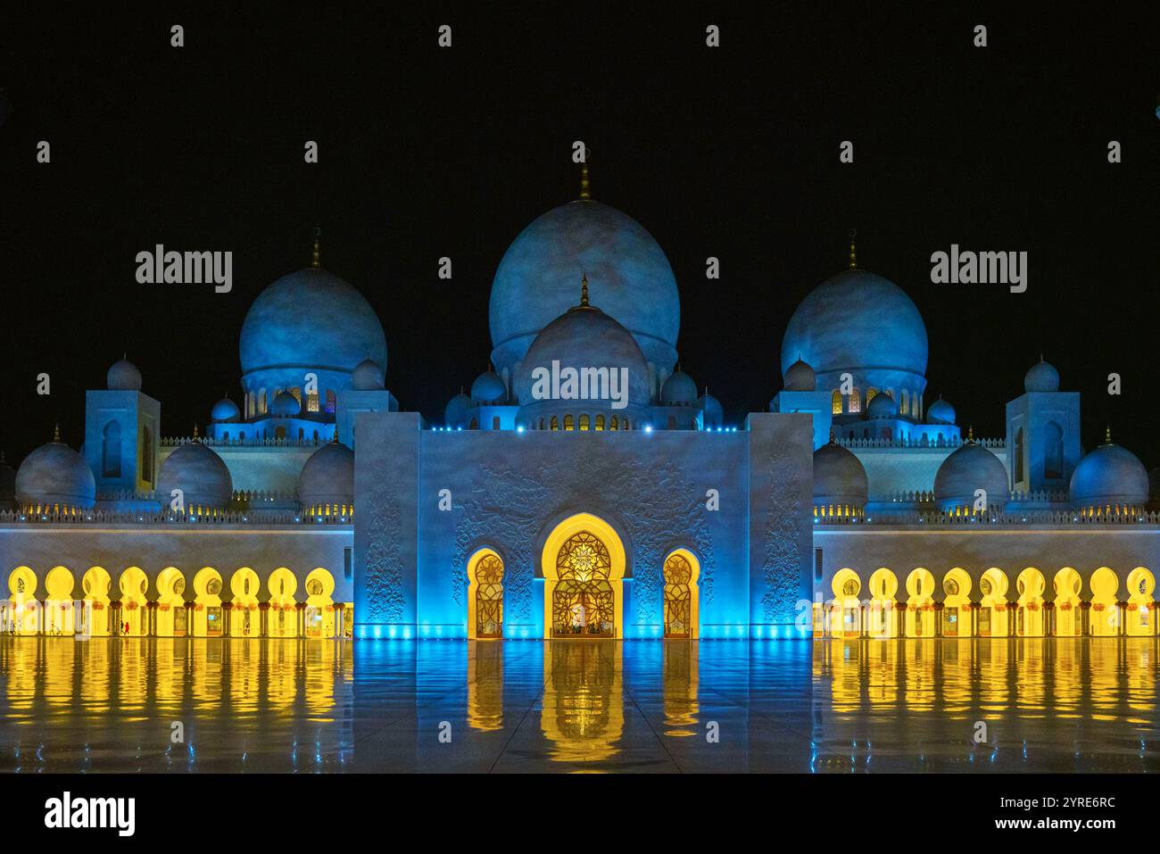 La grande Moschea dello Sceicco Zayed illuminata di notte con luci blu e dorate che si riflettono sul cortile in marmo lucido di Abu Dhabi, Emirati Arabi Uniti. Foto Stock
