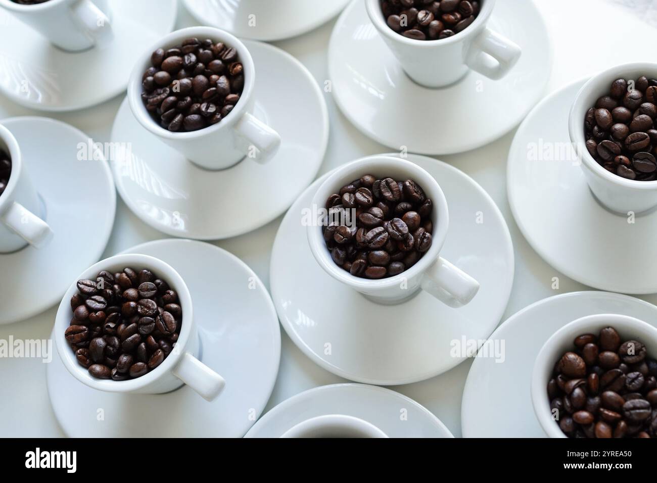 Tazze da caffè bianche con chicchi di caffè disposti su un tavolo bianco Foto Stock