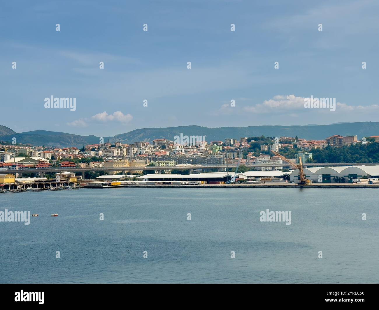 Trieste, Italia - 29 giugno 2024: Porto commerciale. Grandi magazzini sui moli senza navi. Paesaggio urbano e catena montuosa all'orizzonte Foto Stock