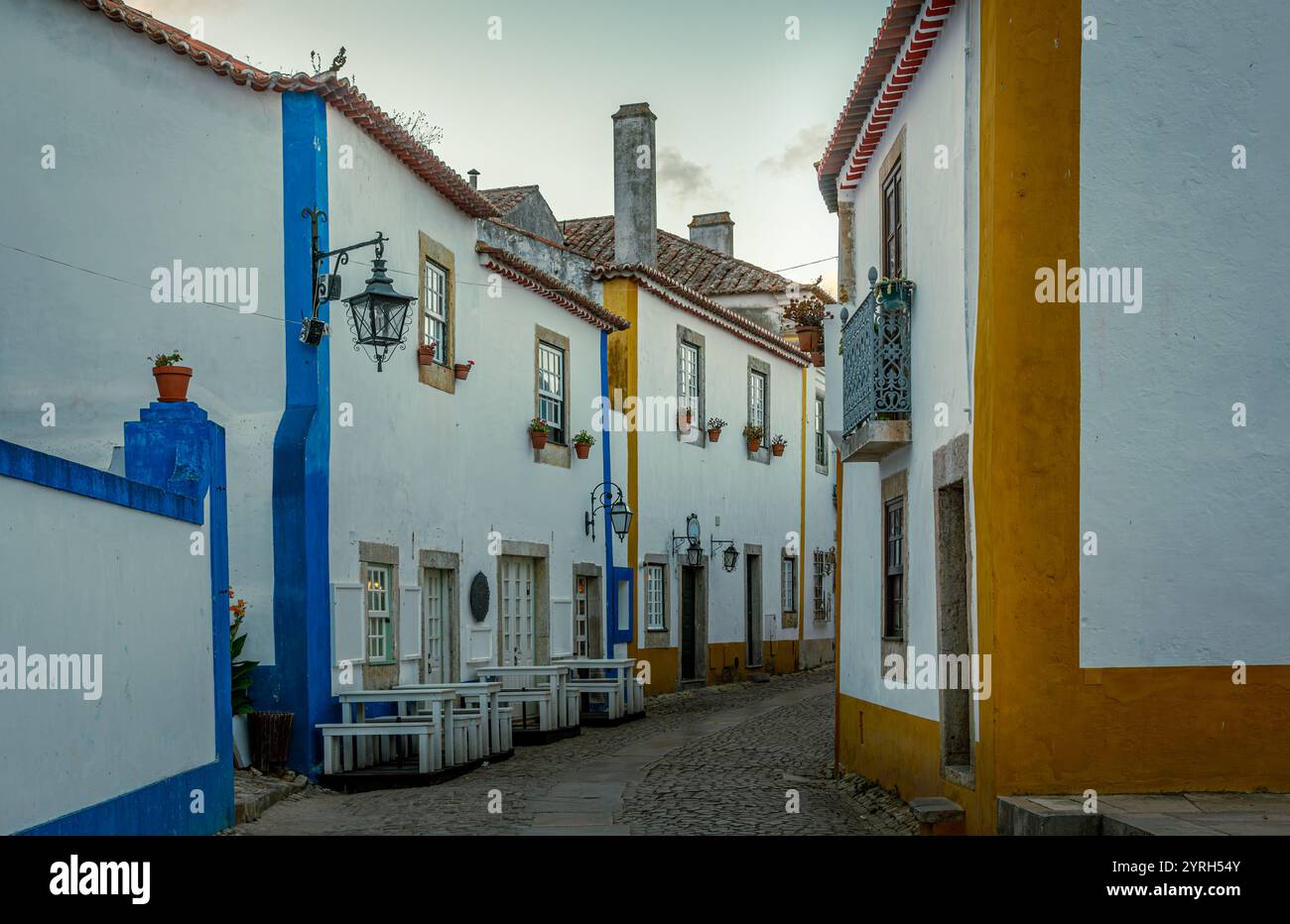 Strada acciottolata che si snoda attraverso la storica città di Obidos in portogallo, caratterizzata da affascinanti case bianche adornate con accenti blu e gialli e Foto Stock