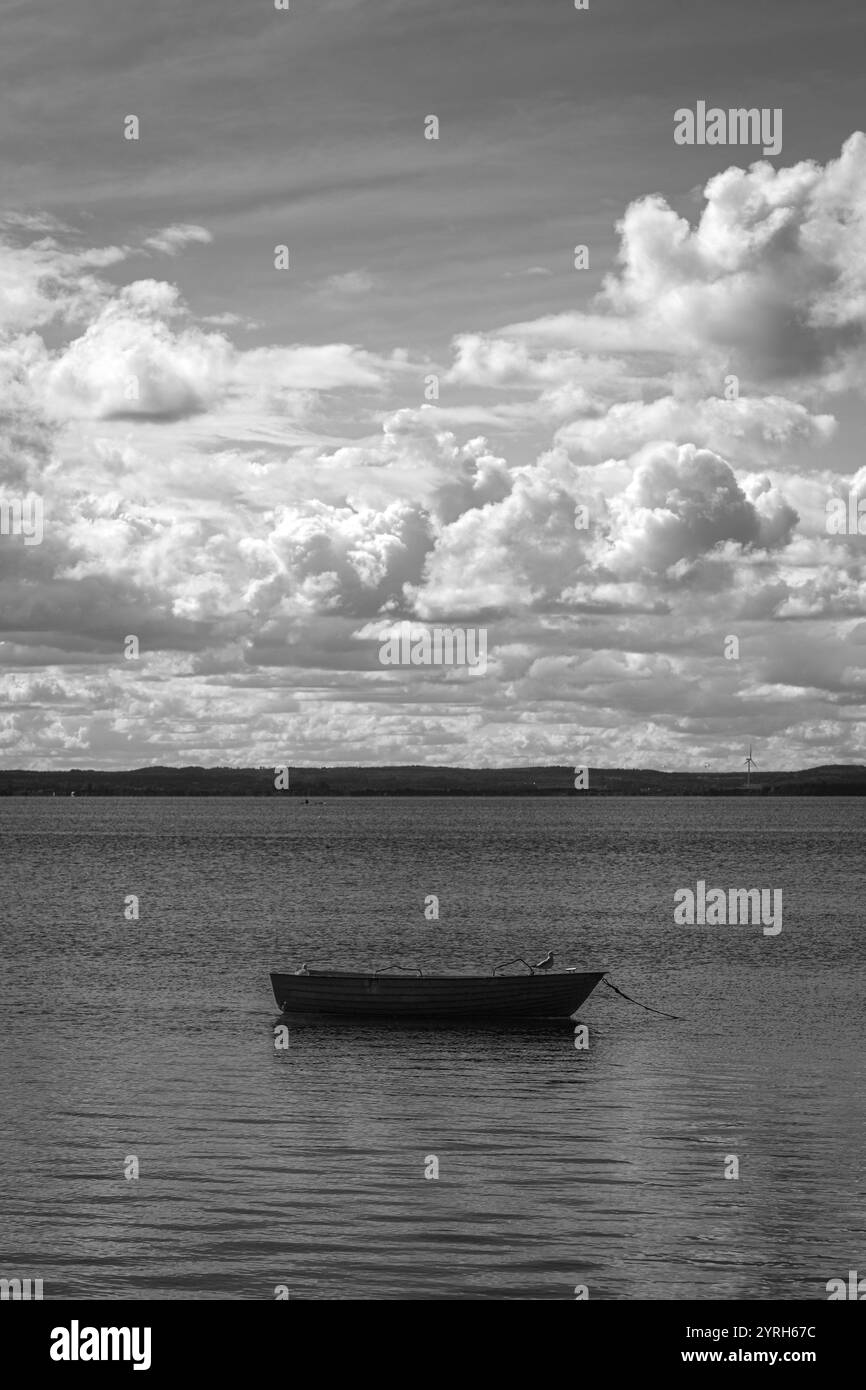 Una piccola barca in legno galleggia sul lago calmo sotto il cielo nuvoloso a chalupi, in polonia, creando una serena e tranquilla fotografia di paesaggi in bianco e nero Foto Stock