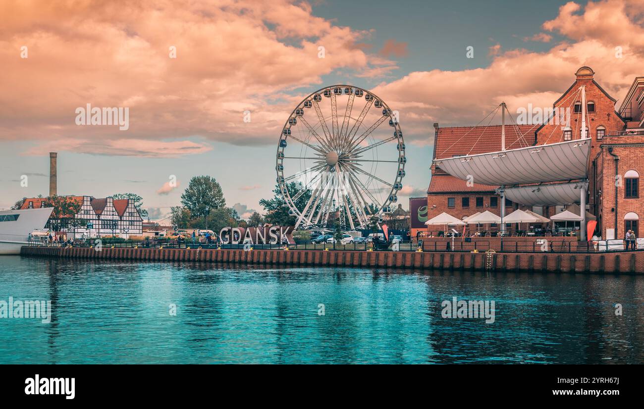 L'iconica ruota panoramica si erge alta lungo il fiume motlawa a danzica. Polonia. Con il nome della città ben visibile mentre il sole tramonta. Foto Stock