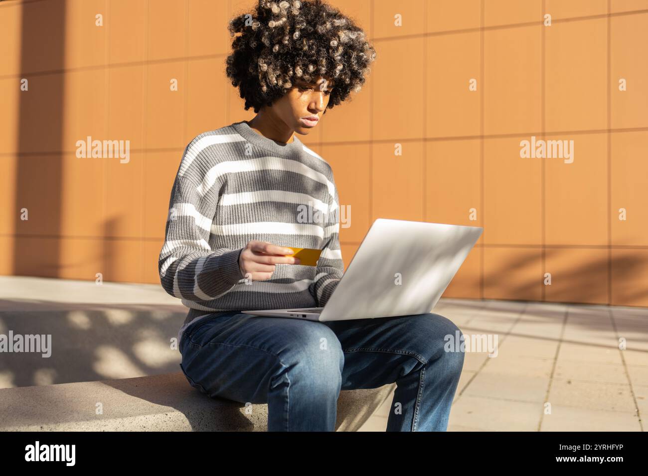 Una donna di razza mista con vitiligine ama trascorrere una giornata rilassante all'università, siede all'aperto con un laptop e una carta di credito, crogiolandosi alla luce del sole contro un Foto Stock