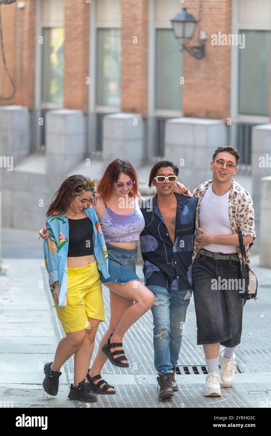 Un allegro gruppo di quattro amici che ridono e camminano per una strada della città, mostrando i loro stili di moda unici con abiti estivi luminosi. Foto Stock