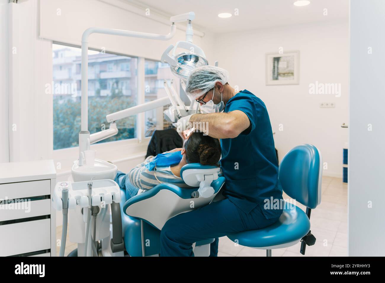 Un dentista frequenta un paziente in una clinica dentale moderna e luminosa. La sedia dentale e le attrezzature sono visibili, sottolineando l'igiene orale professionale in un Foto Stock