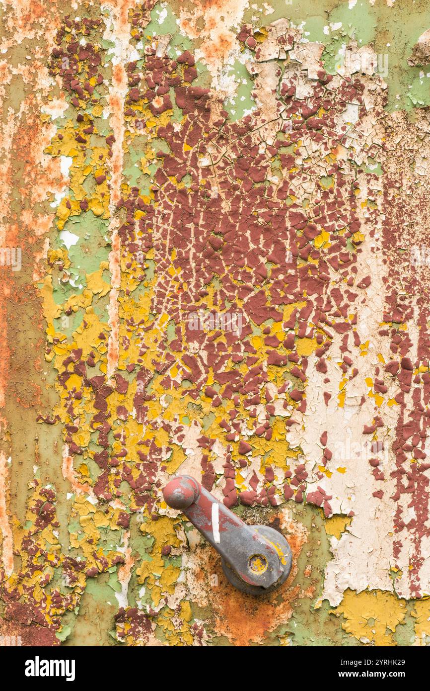 Un primo piano di un manico e metallo usurato con vernice sbucciante nei colori verde, giallo e ruggine la trama e l'aspetto usurato evidenziano il decadimento industriale Foto Stock