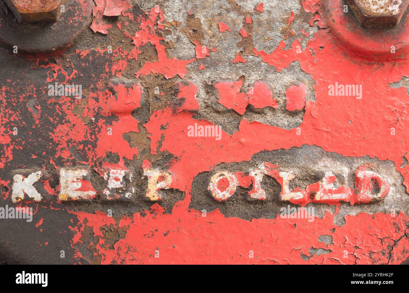 Una vista dettagliata del metallo industriale intemprato con testo in rilievo mantenere oliato la superficie mostra una vernice rossa che si stacca, esponendo ruggine e consistenza Foto Stock