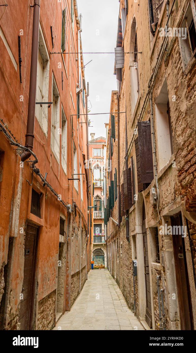 Vicolo pittoresco fiancheggiato da edifici rustici e colorati e finestre con persiane. Le facciate intemperie evocano un senso di storia e fascino, invitante esploratore Foto Stock