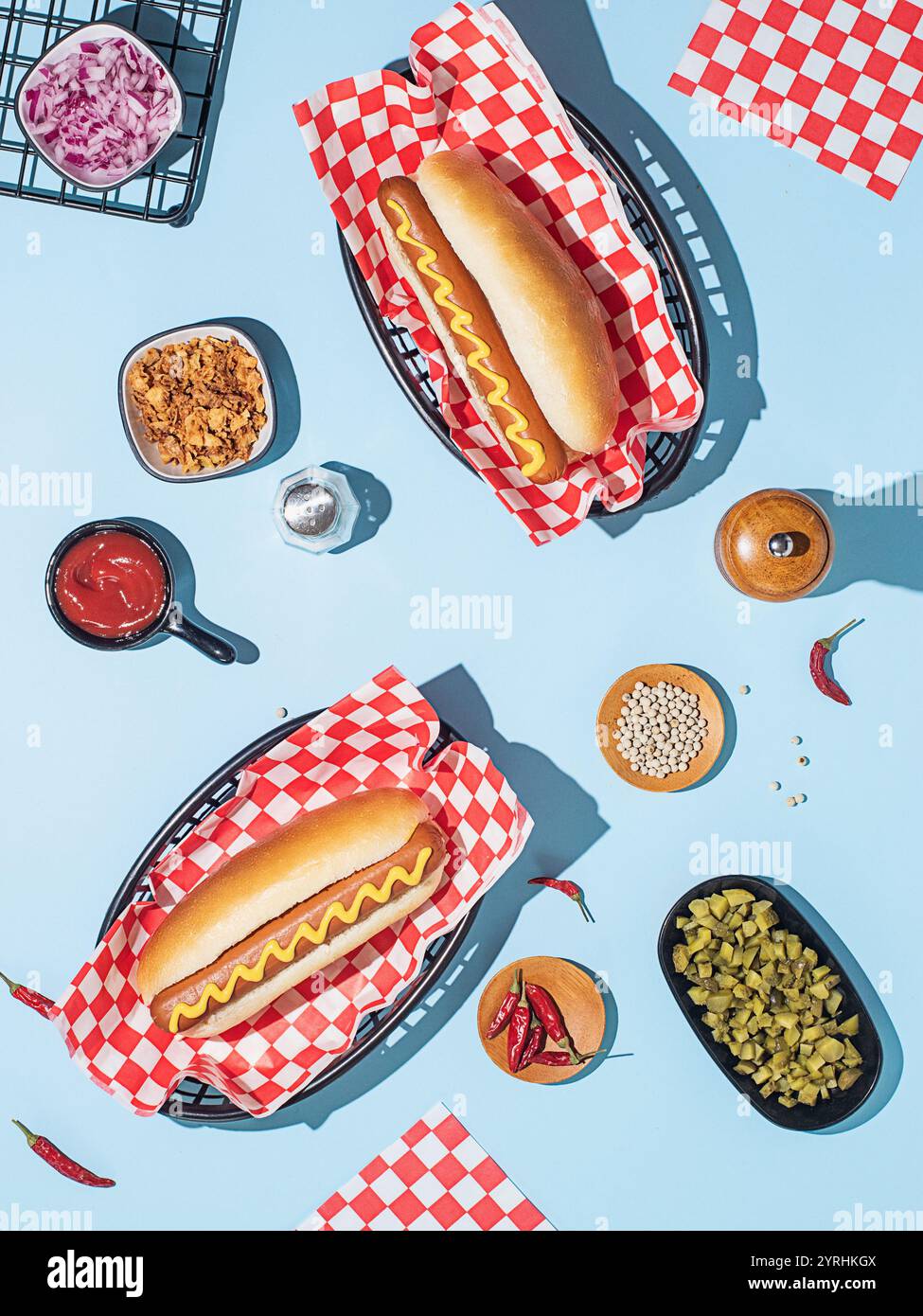 Un piatto di due hot dog classici in panini con senape, disposti con vari condimenti e condimenti su un vivace sfondo blu Foto Stock