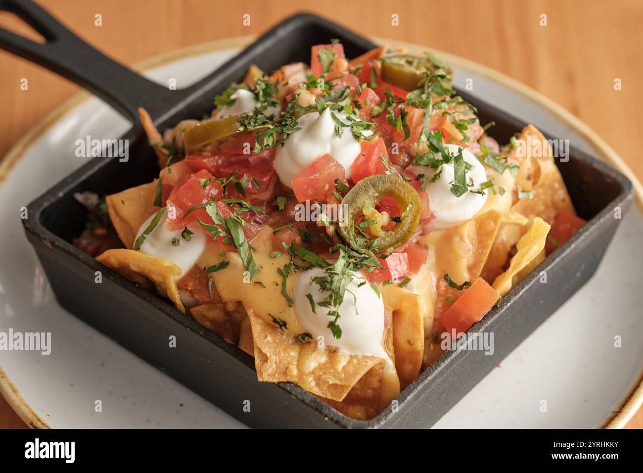 Primo piano di nachos salati ricoperti di formaggio fuso, salsa fresca, panna acida, jalapenos e coriandolo, servita in una padella nera perfetta per uno spuntino Foto Stock