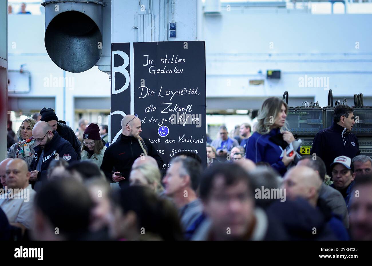 Wolfsburg, Germania. 4 dicembre 2024. I dipendenti della casa automobilistica tedesca Volkswagen (VW) stanno intorno a una targa che riporta "in memoria silenziosa" mentre partecipano a una riunione di lavoro presso la sede centrale della Volkswagen a Wolfsburg, in Germania. I lavoratori della Volkswagen in tutta la Germania sono bloccati in una crescente disputa sul lavoro per la casa automobilistica tedesca colpita dalla crisi, con migliaia di posti di lavoro in gioco. Credito: Ronny Hartmann/AFP POOL/dpa/Alamy Live News Foto Stock