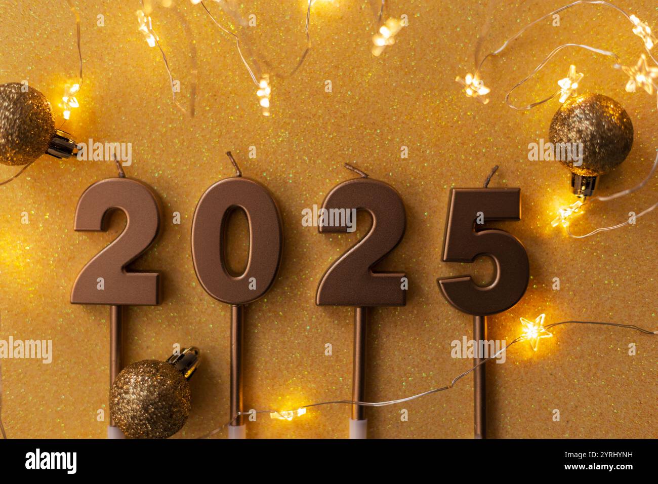 Le candele dorate festive 2025 con stelle luminose giacciono con palline dorate su sfondo dorato. Carta da parati per le vacanze. Capodanno 2025 e cartolina di Natale Foto Stock