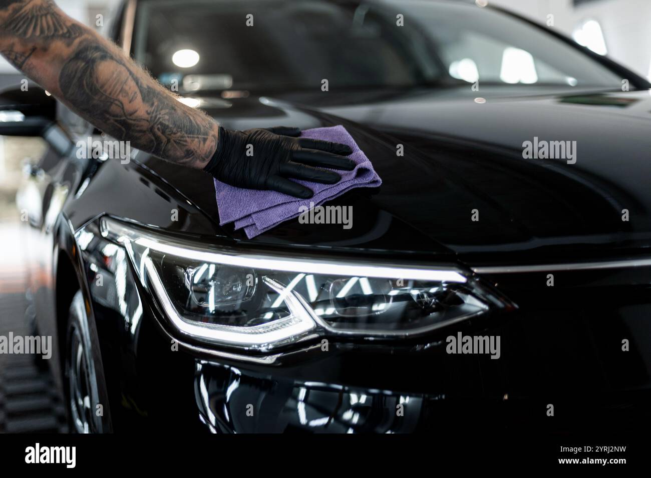 Uomo professionista che pulisce l'auto con microfibra in garage. Studio di dettaglio, cura dell'auto. Lucidatura auto Foto Stock
