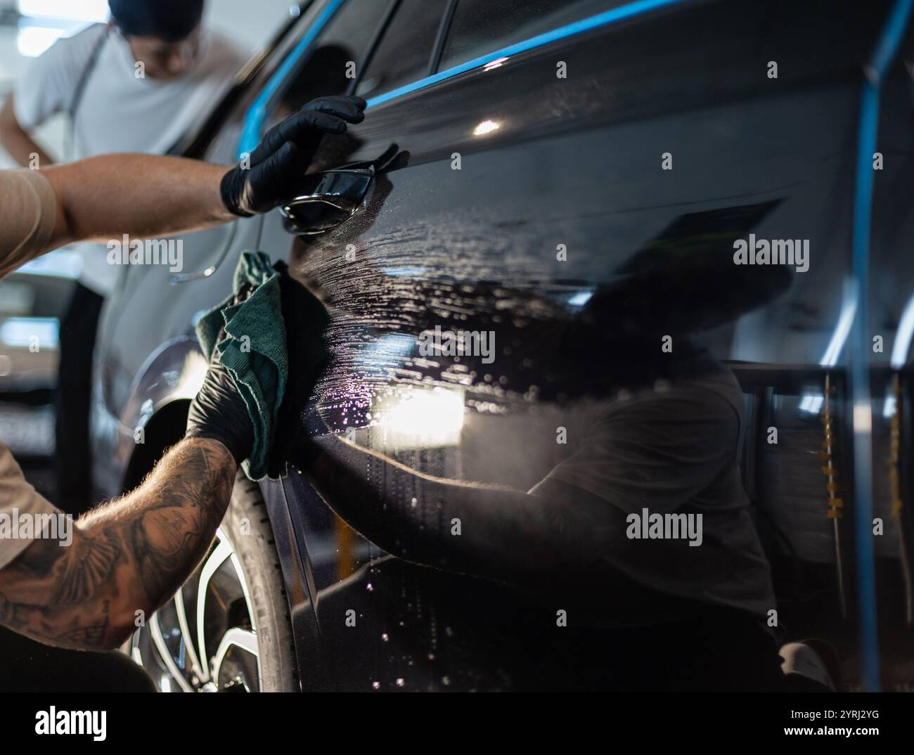 L'autolavaggio MAN lava l'auto e pulisce l'auto nera con uno straccio nello studio di dettaglio Foto Stock