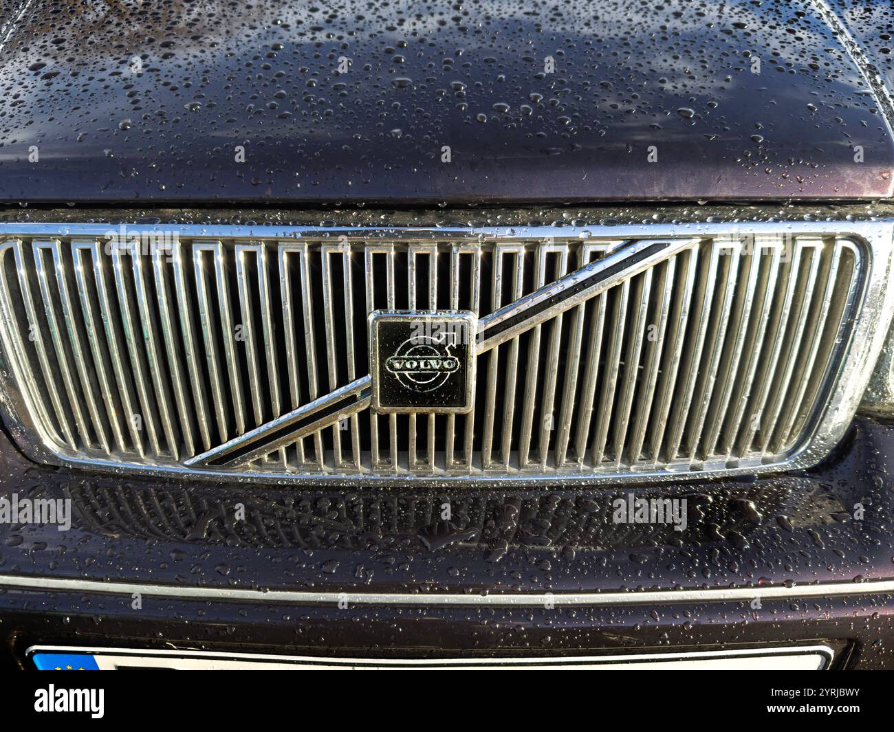 Primo piano di una classica griglia per auto Volvo V90 vintage con gocce di pioggia e l'iconico logo circolare con finitura metallizzata - Immagine stock catturata con smartphone