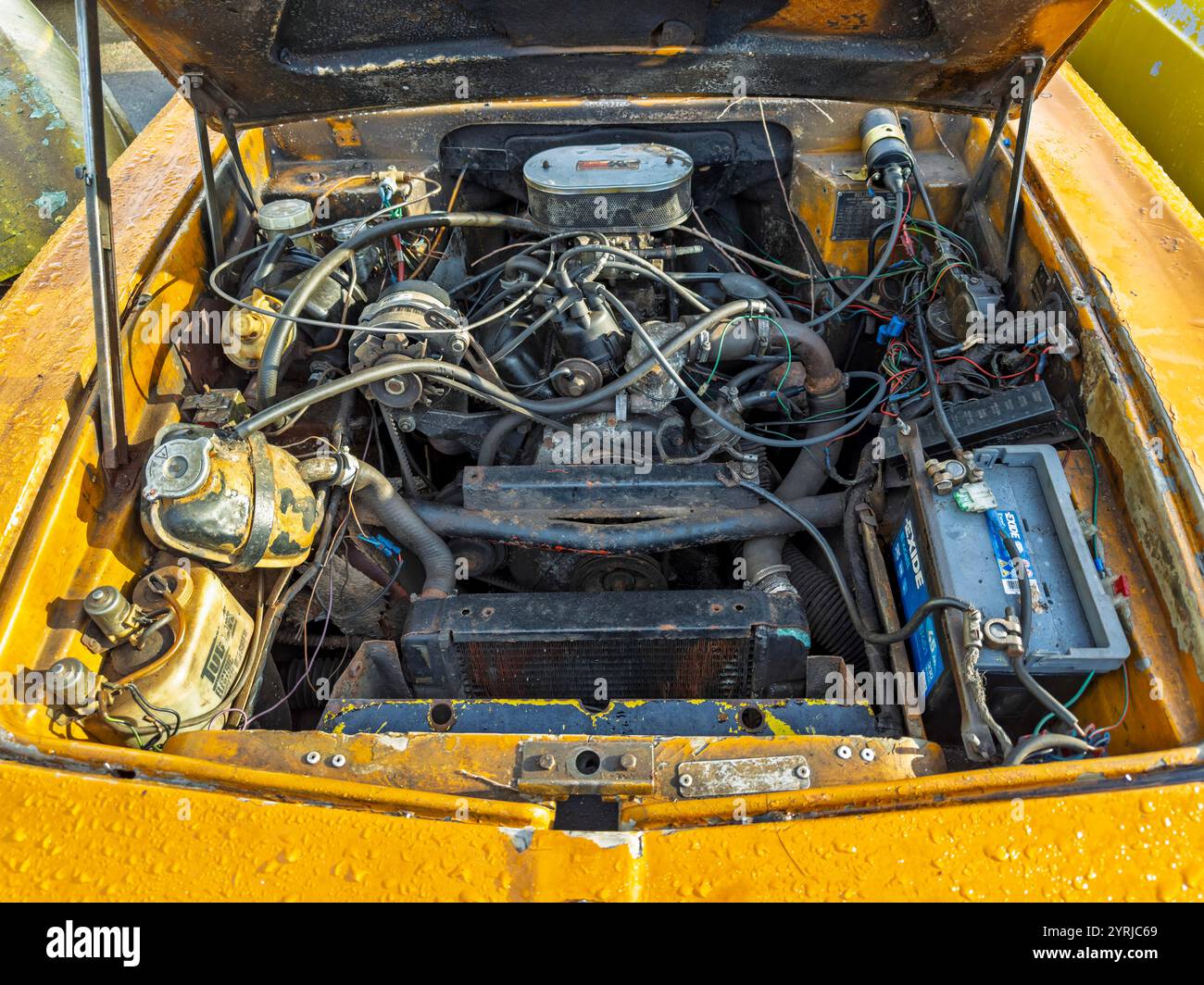 Motore per auto Reliant Scimitar GTE vintage 1972 in un veicolo giallo con cofano aperto, che mostra i componenti e il cablaggio dettagliati per il restauro automobilistico. Foto Stock