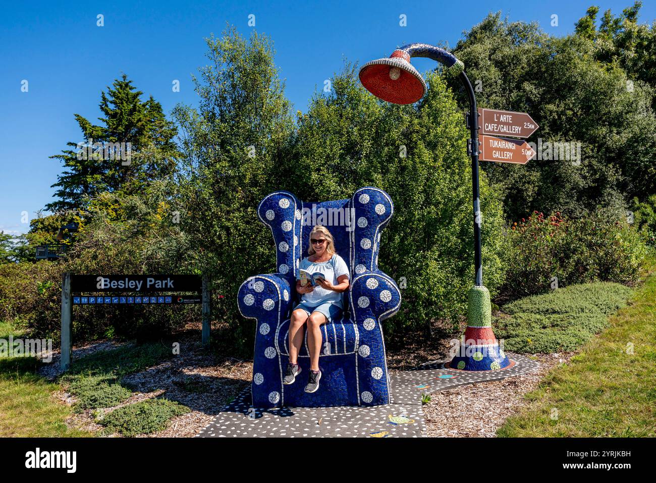 A Female Tourist siede su Una sedia Mosaic Reading A Book, Besley Park, Taupo, nuova Zelanda. Foto Stock