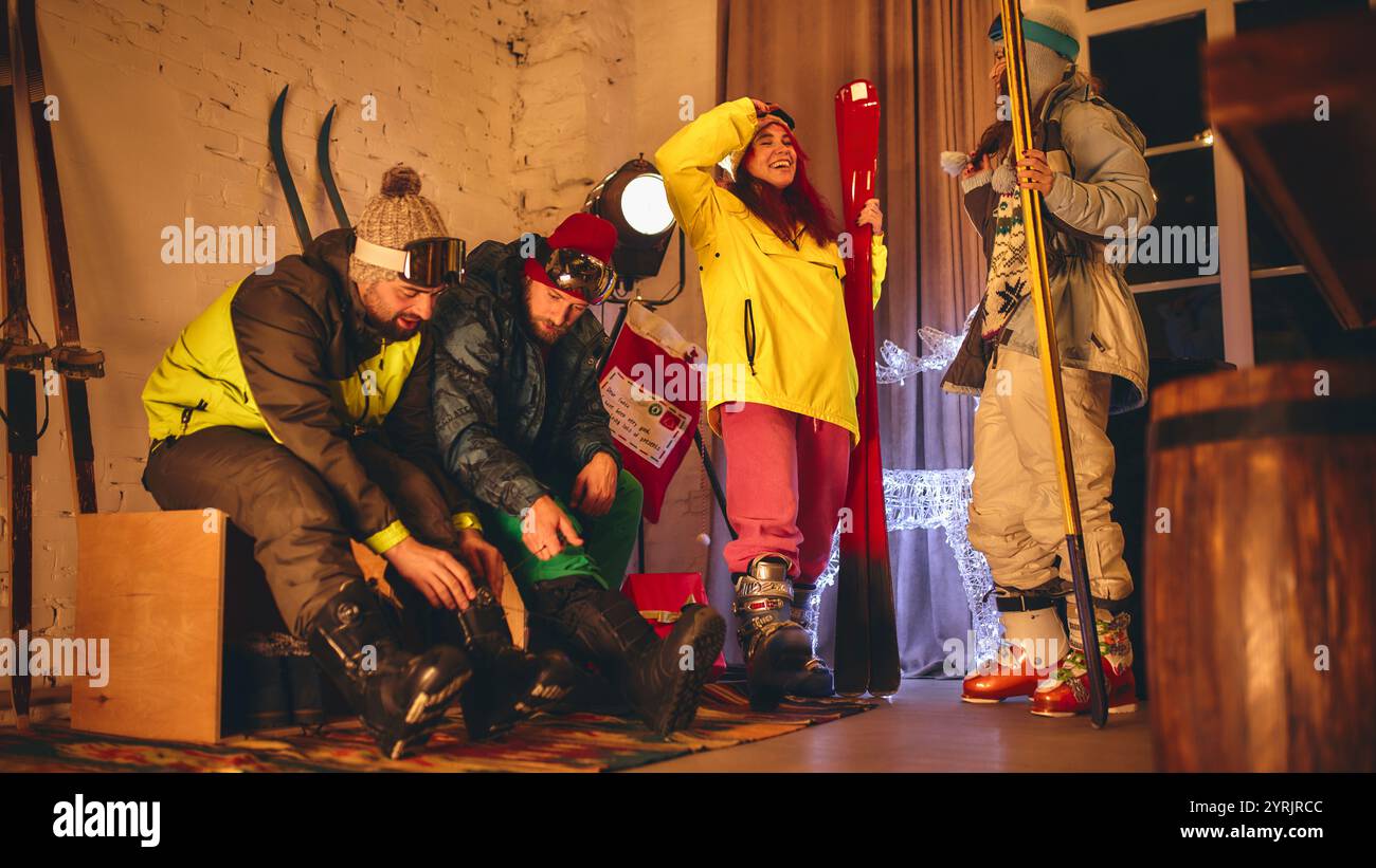 Il gruppo si prepara a sciare all'interno, stringendo gli stivali e controllando l'equipaggiamento, con abiti vivaci e allestimenti natalizi di luci e decorazioni. Foto Stock