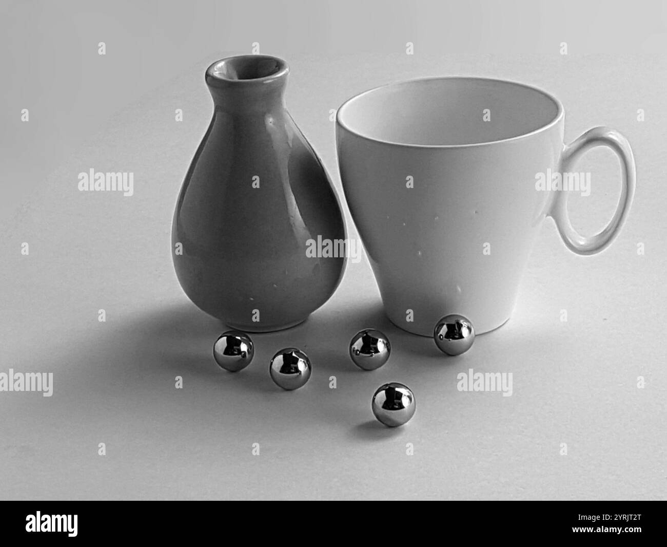 Una straordinaria fotografia monocromatica STILL-Life con tazza in ceramica bianca, vaso liscio e sfere metalliche riflettenti disposte artisticamente. Foto Stock