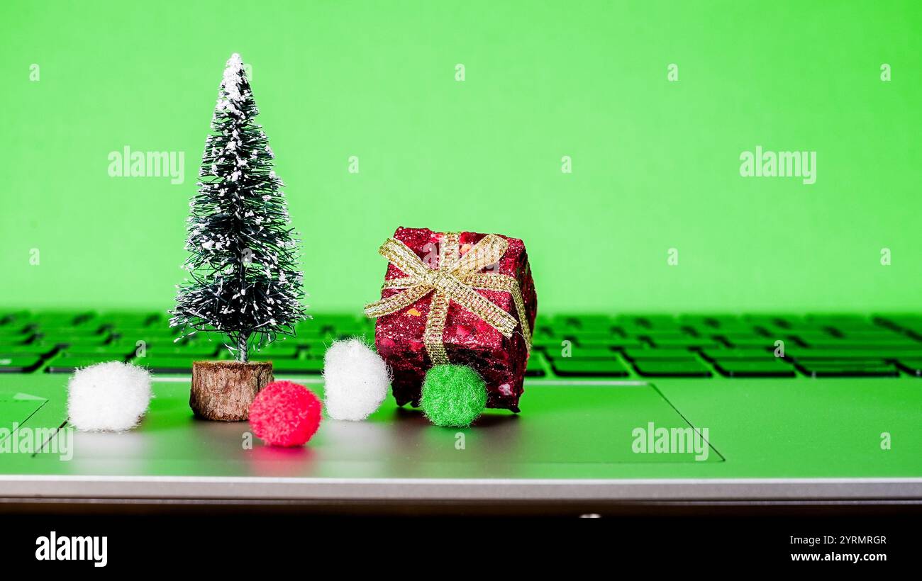 L'albero di Natale in miniatura e i regali adornati si trovano sulla tastiera del computer portatile, creando un'atmosfera allegra per la preparazione delle vacanze. Foto Stock