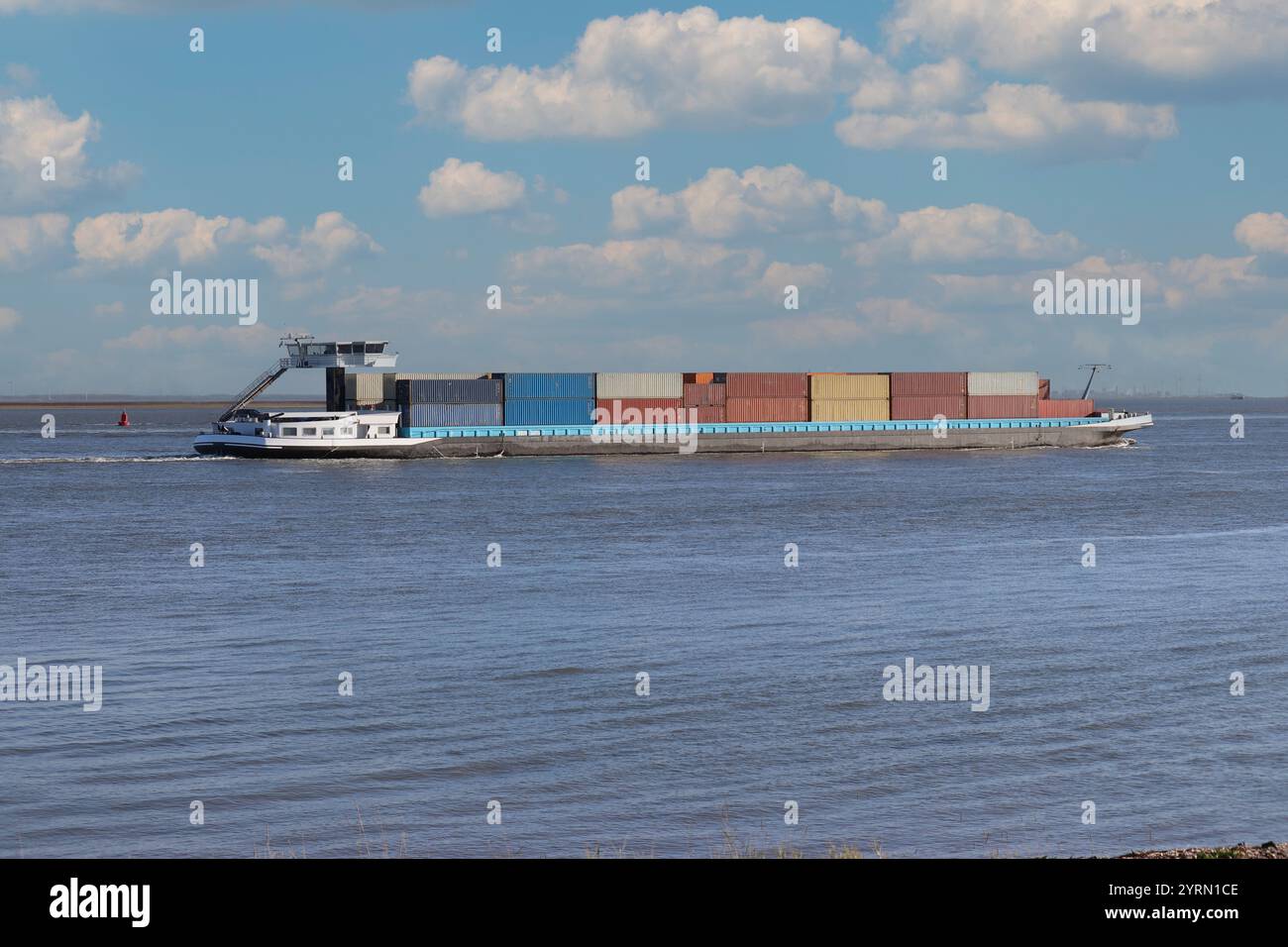 una chiatta portacontainer sta navigando nel mare occidentale della schelda verso il porto di anversa e un cielo blu con nuvole Foto Stock