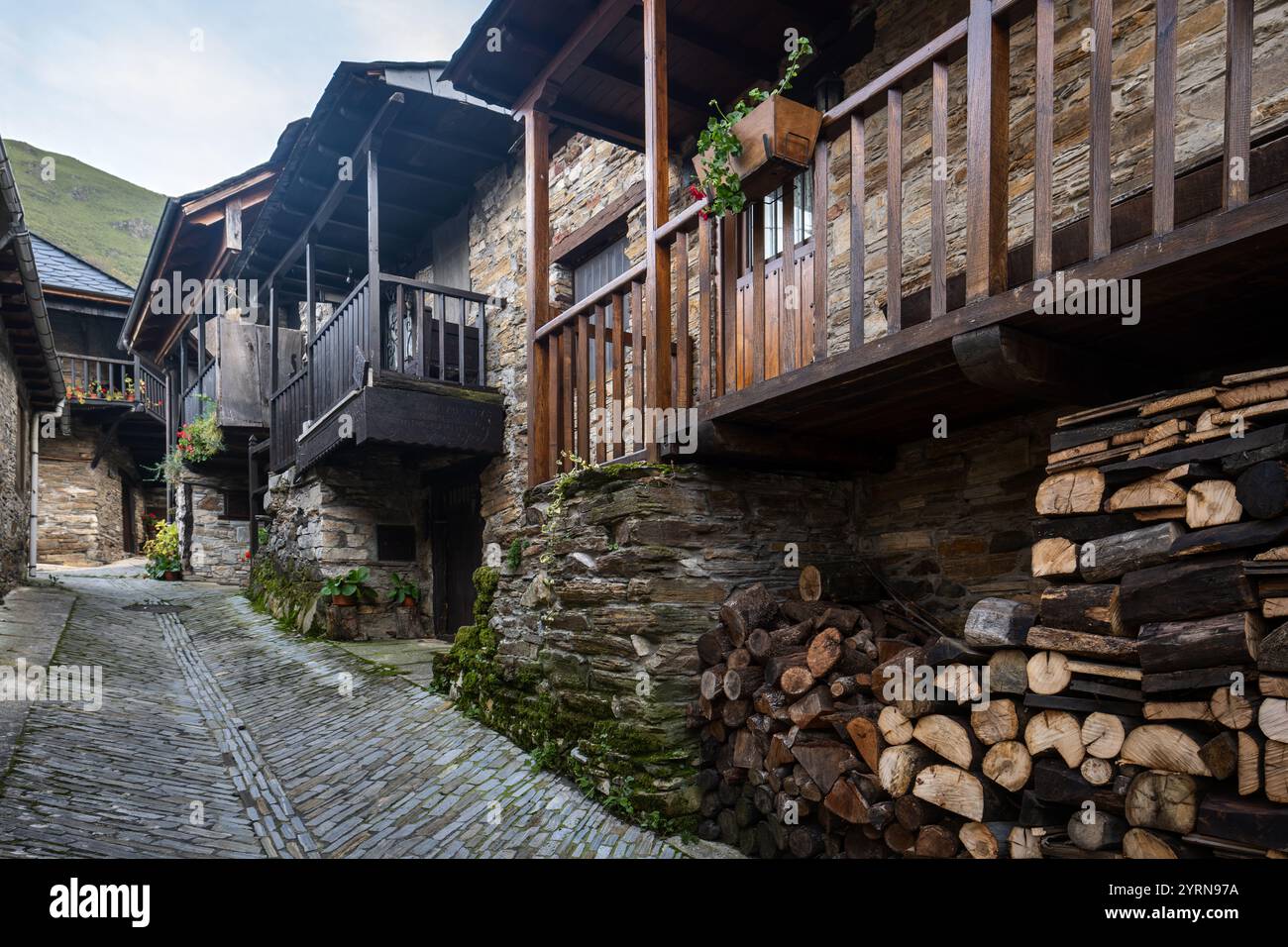 Case in pietra con balconi in legno che costeggiano una stretta strada acciottolata in un villaggio di montagna Foto Stock