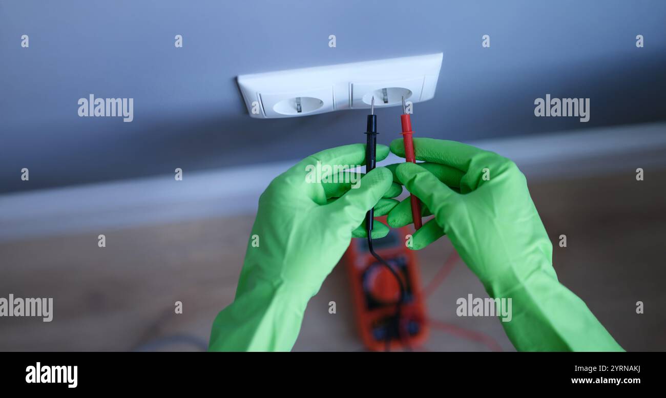 Le mani con i guanti tengono un multimetro digitale vicino alla presa Foto Stock