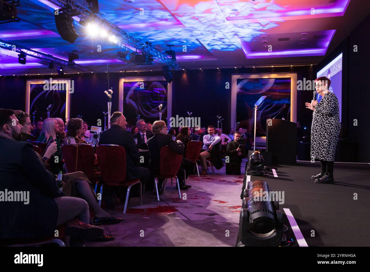 Jo Brand parla con un microfono a una grande sala di persone che cenano Foto Stock