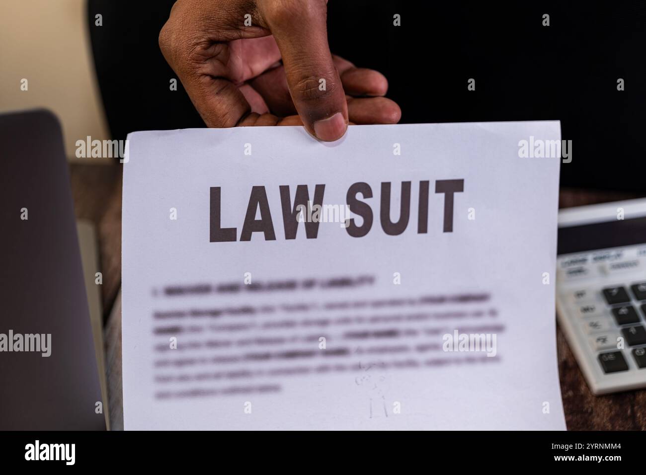 Una mano tiene in mano un documento di causa, suggerendo problemi legali. La calcolatrice e il notebook suggeriscono implicazioni finanziarie. Foto Stock