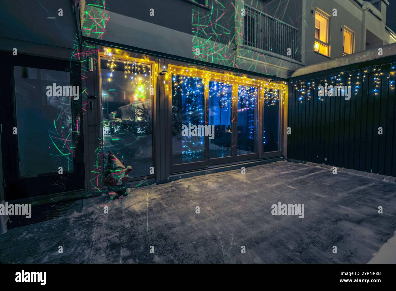 Esterno della casa festiva con colorate luci natalizie che si riflettono sulle finestre durante la nevosa sera invernale. Svezia. Foto Stock