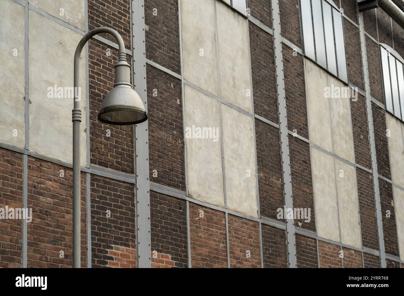 Lampione stradale in metallo che illumina la facciata di un vecchio edificio industriale con pareti in mattoni e cemento Foto Stock