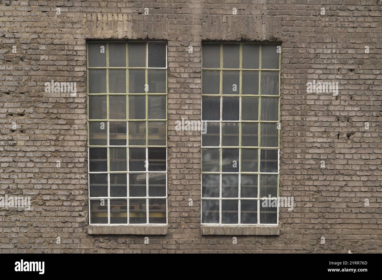 Due grandi finestre industriali con piccoli pannelli e telai metallici sono collocate in una vecchia parete di mattoni, rivelando i pallet all'interno dell'edificio Foto Stock