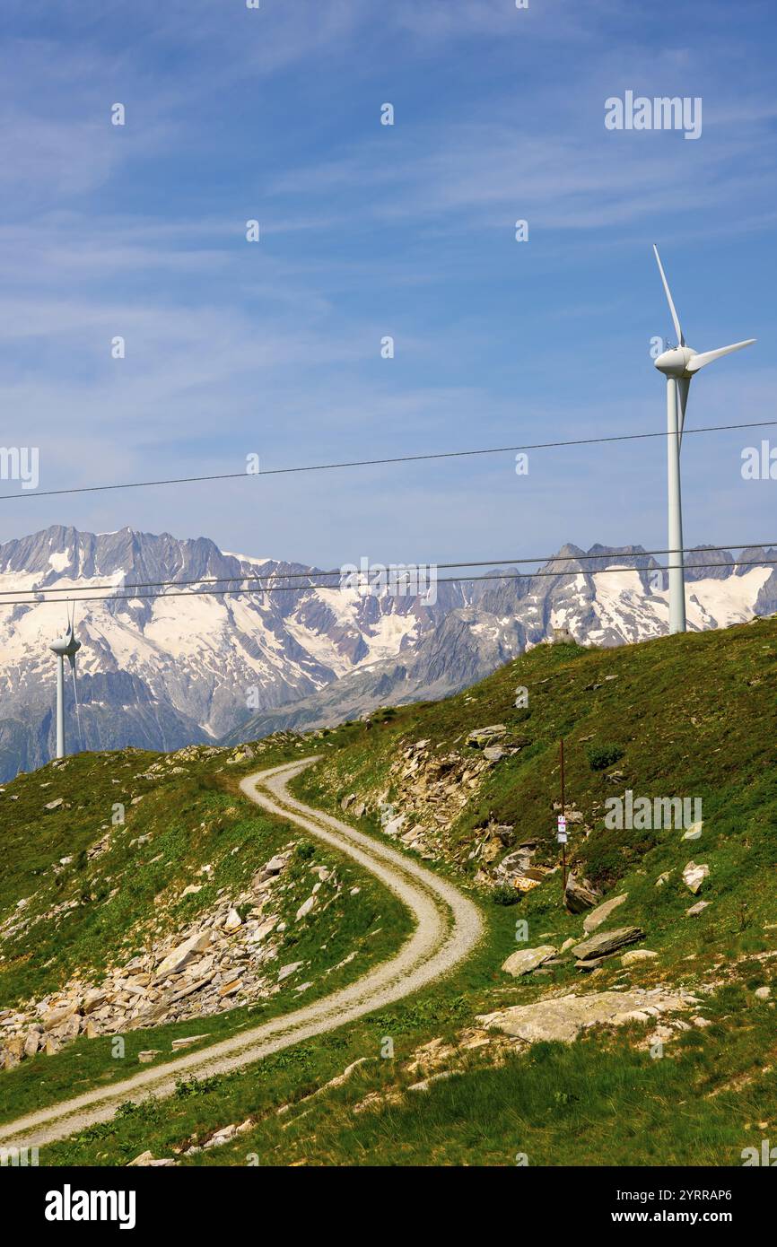 Turbina eolica e montagna con ghiacciaio e funivia sopraelevata e cielo blu e nuvole in una giornata estiva soleggiata ad Andermatt, Uri, Svizzera. Foto Stock