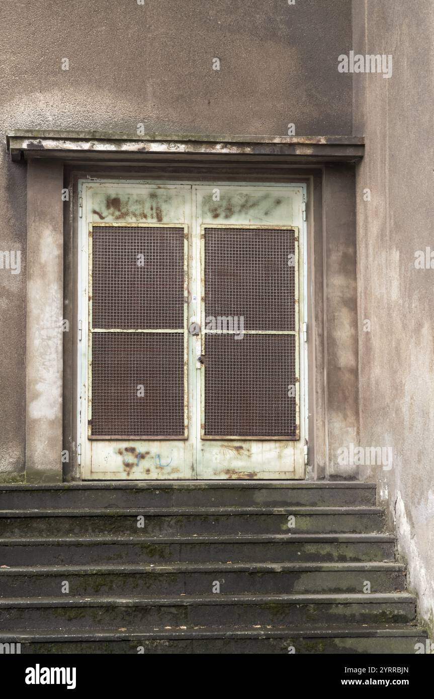 Griglia metallica arrugginita che protegge l'ingresso di un vecchio edificio con scale in cemento e facciata intemprata Foto Stock