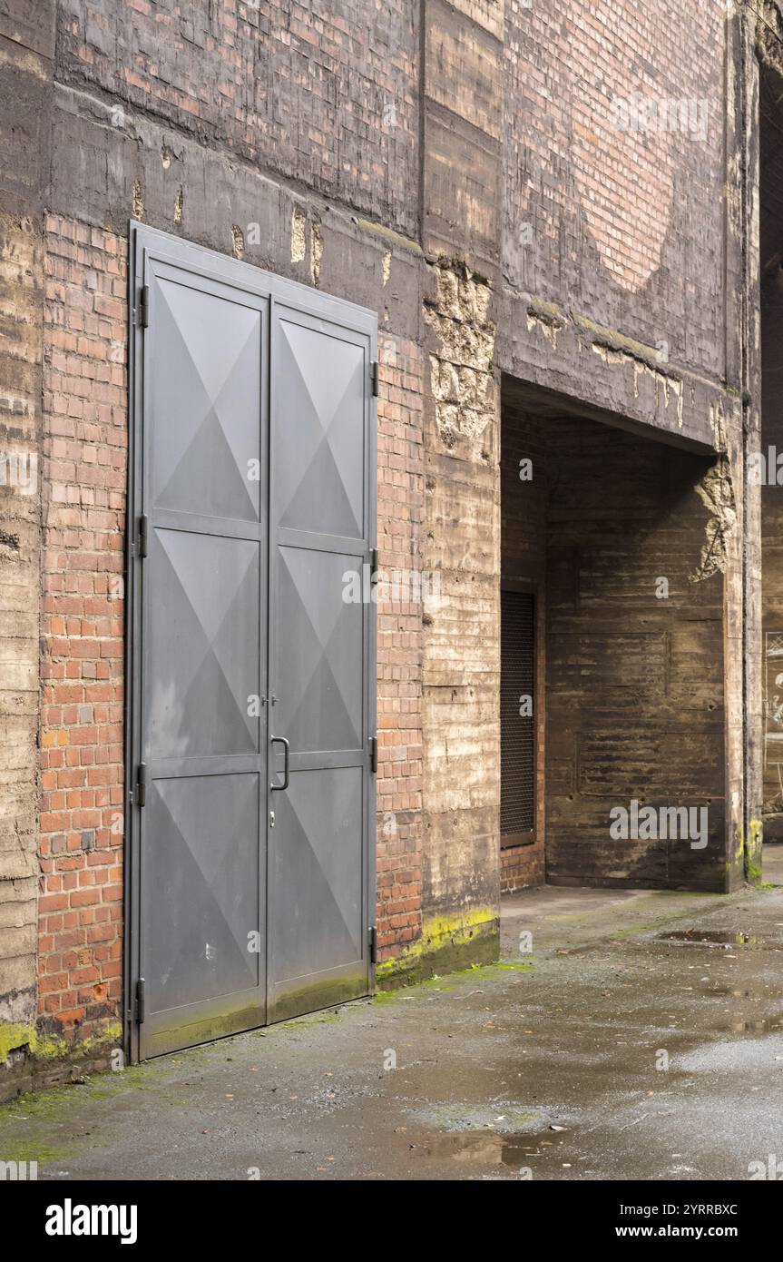 Porta metallica chiusa che blocca l'accesso all'edificio industriale in decadenza con pareti in mattoni danneggiate Foto Stock