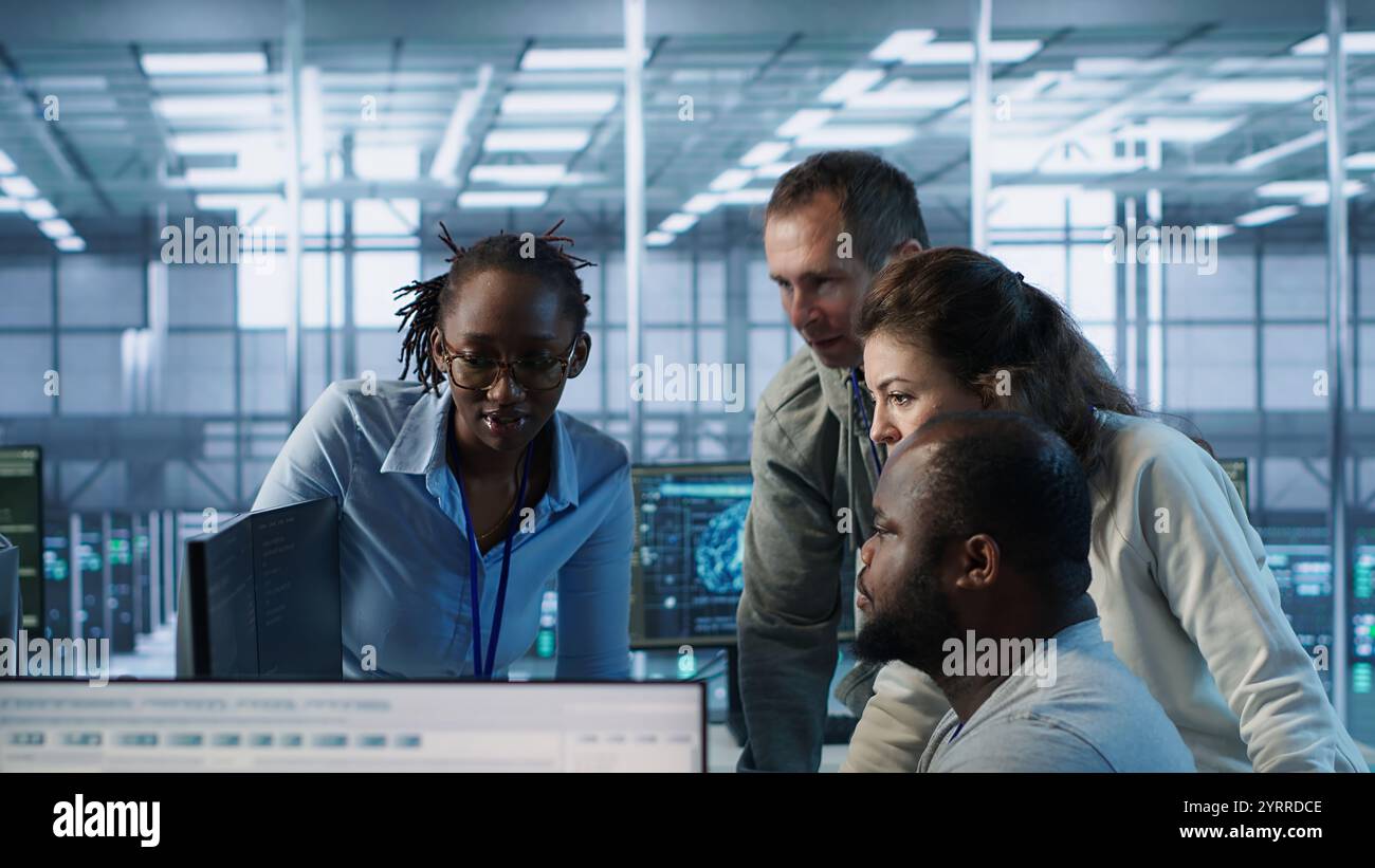 Team multietnico di ingegneri che lavorano nell'hub server, utilizzando i PC per analizzare i dati. Gruppo multirazziale di dipendenti che esaminano l'infrastruttura nel data center, garantendo l'integrità e la sicurezza del sistema, telecamera A. Foto Stock